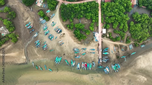 Top-down aerial drone view of a traditional fishing harbor along the Konkan coast of India, showing colorful fishing boats anchored on a sandy beach near calm coastal waters. 