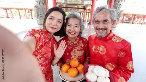 Asian senior couple and daughter in cheongsam qipao dress are having video call to relatives at temple during Chinese new year for family and cousin gathering in hometown	