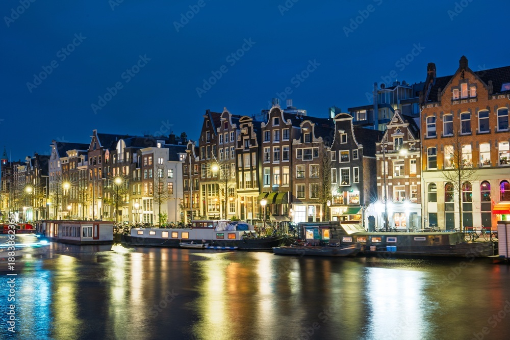 Obraz premium Discover the enchanting nights of Amsterdam, Netherlands, where historic buildings shine on the tranquil canals. A perfect scene for travel enthusiasts and showcasing the city s charm.