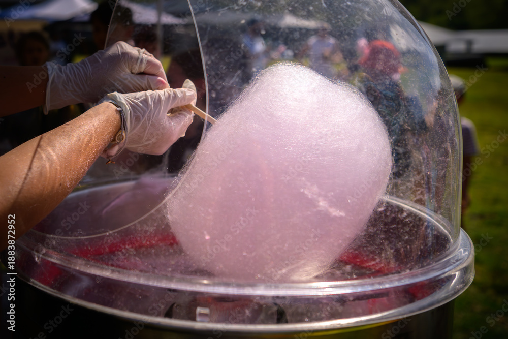 Naklejka premium Hands spinning pink fairy floss at a country fair, giving a sense of whimsy and little kid excitement - horizontal