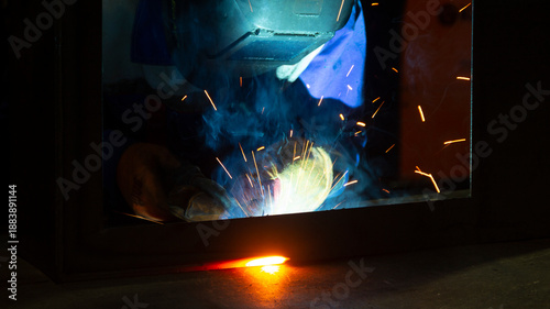 Manual metal welding, welding work in a mask, welding arc, sparks in the dark, bright flash of a welding arc, industrial welding in a protective suit, welding mask