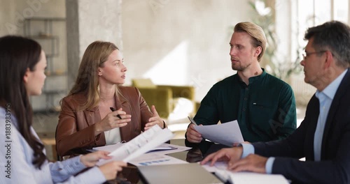 Female team leader explains business strategy, guides colleagues through project details during corporate meeting, group reviewing documents, analyzing data, collaborates on decision making in office