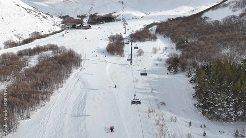 High angle 4K drone footage of a ski resort with ski lifts, and people skiing down a wide mountain slope.