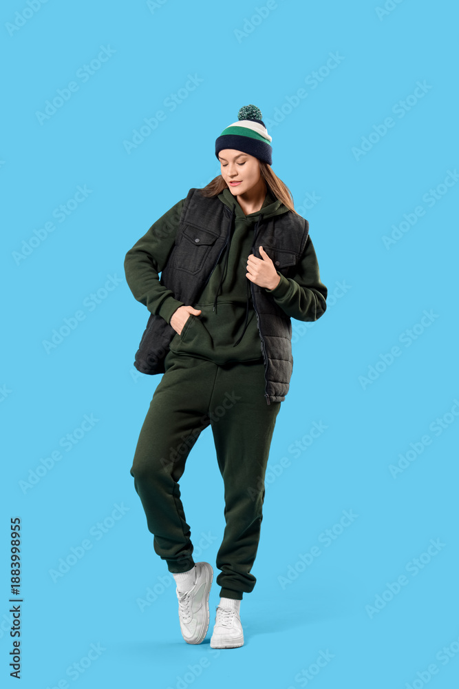 Naklejka premium Young woman in sports suit with warm hat on blue background