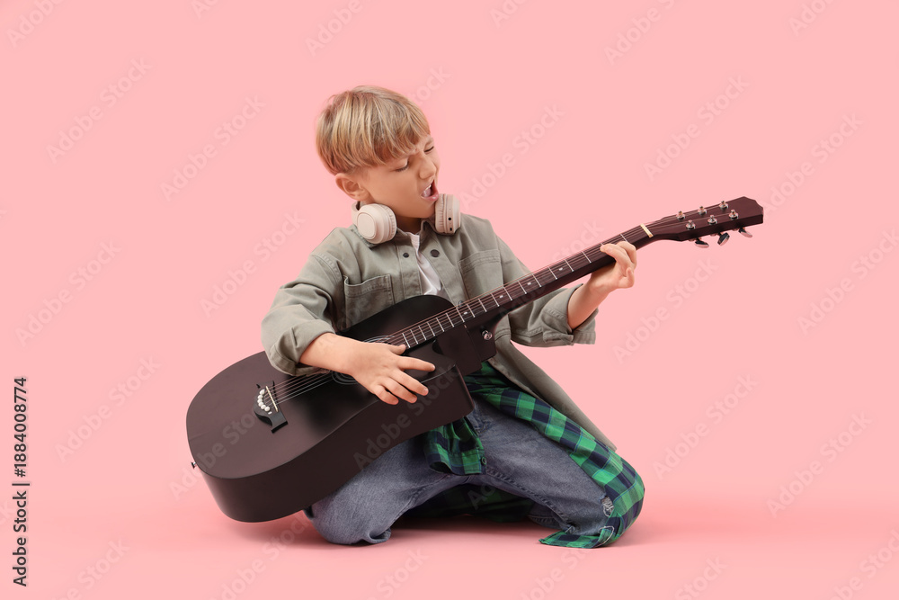 Fototapeta premium Little boy playing guitar on pink background