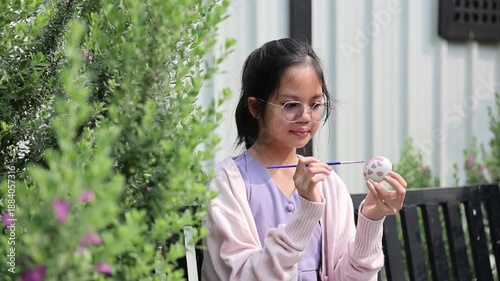 Young asian kid is painting rabbit bunny on easter egg in the outdoor garden for celebrating season festive