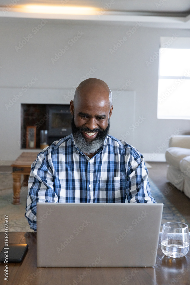 Naklejka premium Mature African American man plaid-shirt sitting at table using silver laptop phone in living room