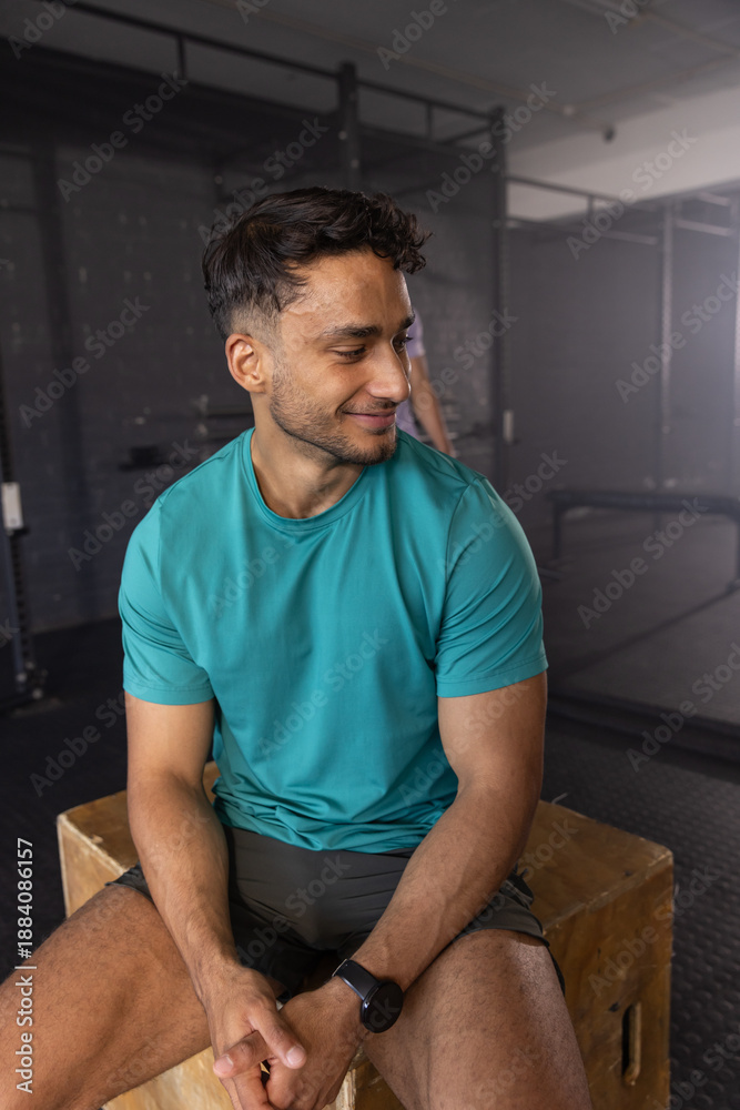 Obraz premium South Asian adult male sitting on plyometric box by pull-up rig in gym area, checking smartwatch