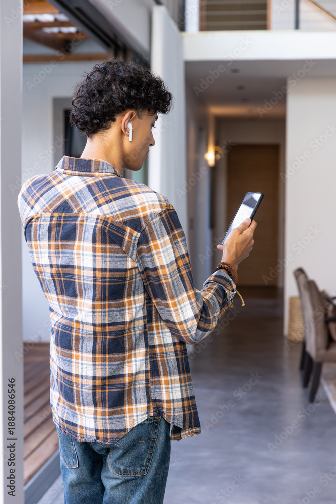 Fototapeta premium Smartphone and wireless earbuds on man near sliding glass door in modern hallway