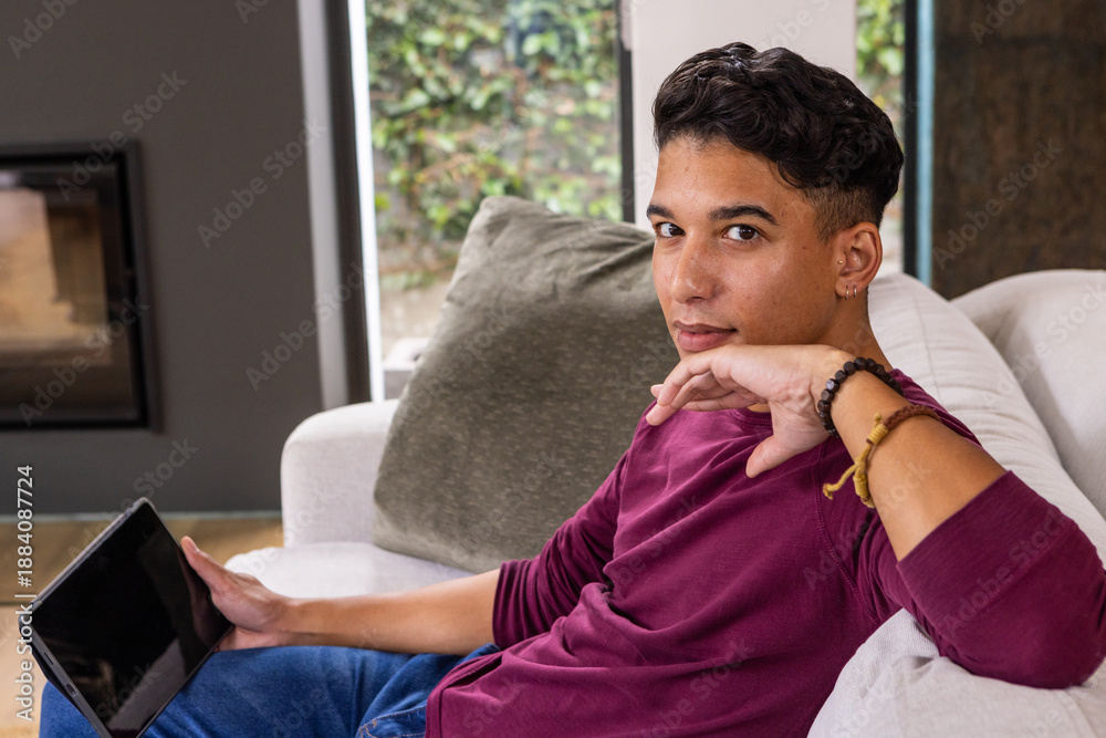 Naklejka premium Man sitting on light grey sofa holding tablet in living room with fireplace insert, windows