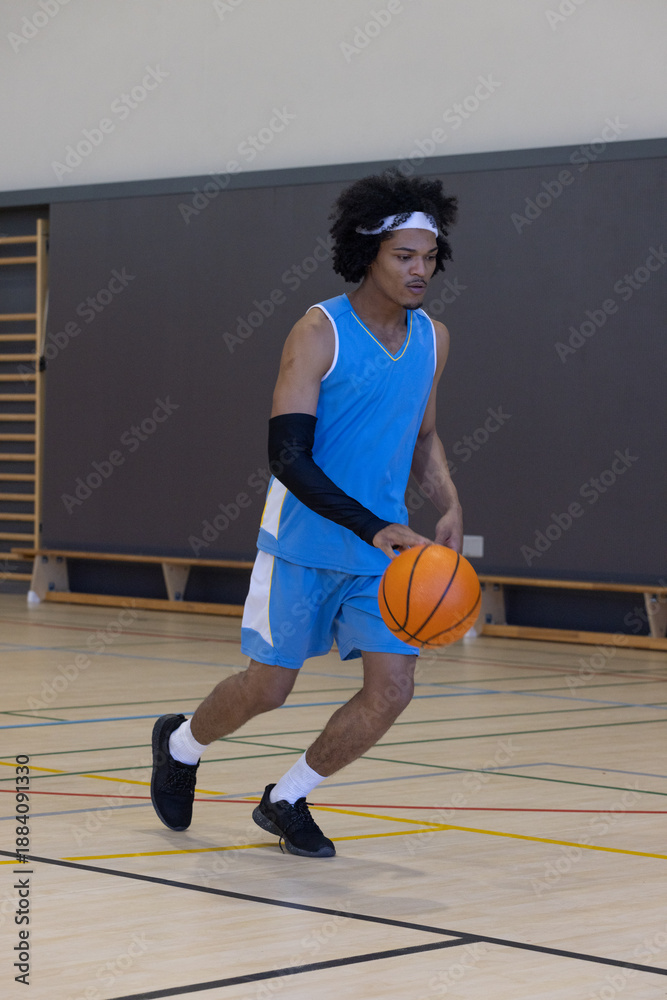 Obraz premium African american man dribbling basketball across court in gym wearing jersey