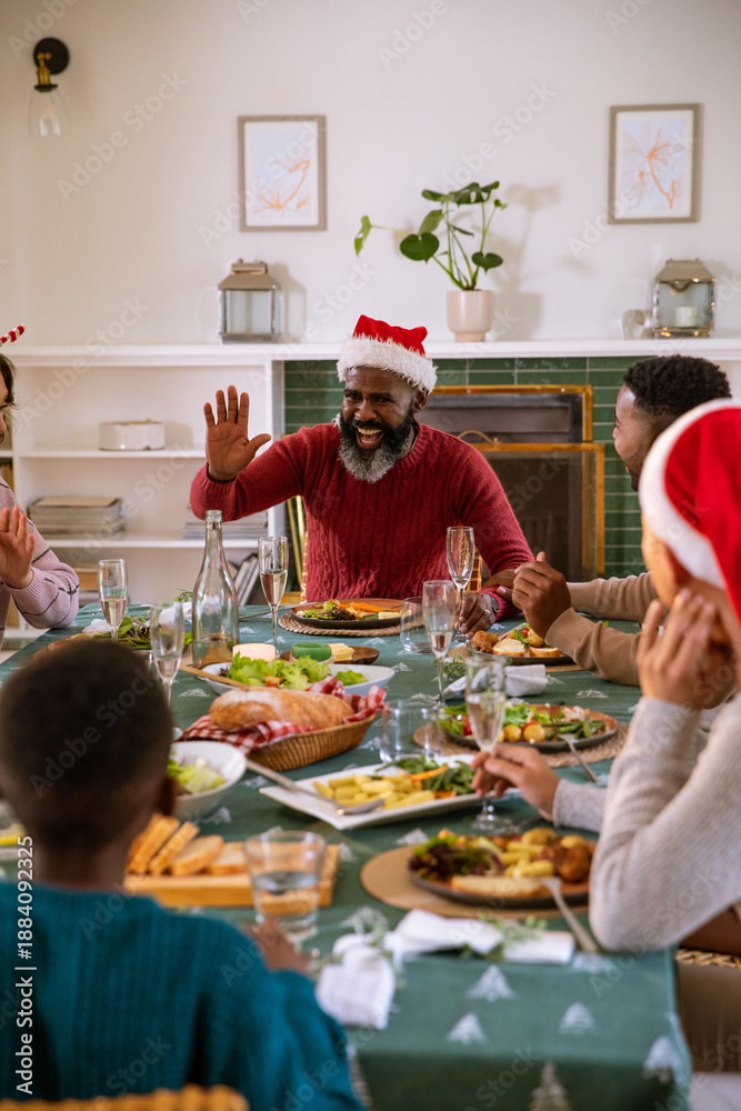 Obraz premium African american family sharing meal wearing santa hats in dining room at table on tablecloth
