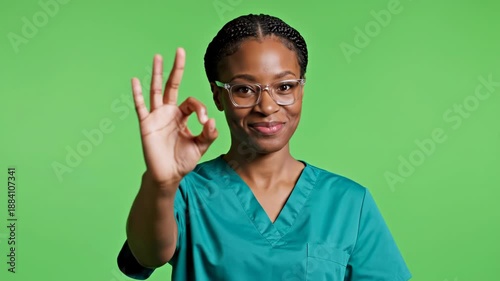 Smiling woman in teal scrubs and glasses gives an 'okay' hand gesture