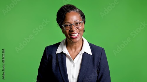 A woman in a dark suit and glasses stands before a vibrant green backdrop