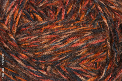 A close up macro shot showing the detailed texture of a variegated brown and orange wool yarn ball filling the entire frame