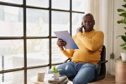 Bilde på lerret Senior black man working from home, focused on a difficult phone call while revi