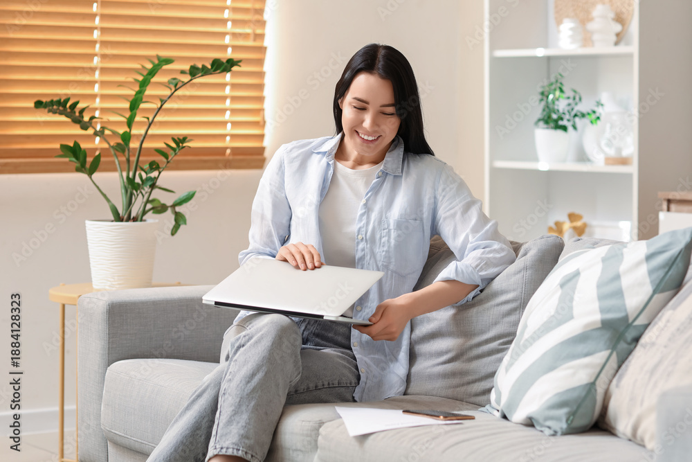 Fototapeta premium Young woman with laptop sitting on sofa at home. Refund concept