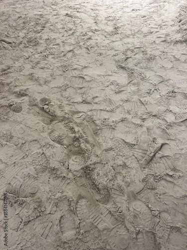 Textured surface of light sand covered with overlapping footprints. The random patterns create a natural abstract background