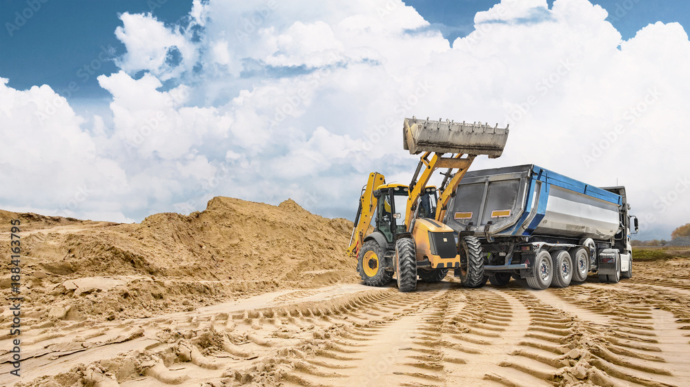 Fototapeta premium Deep tracks from heavy machinery cut through sandy ground with a large sand pile in the background showing ongoing construction activity