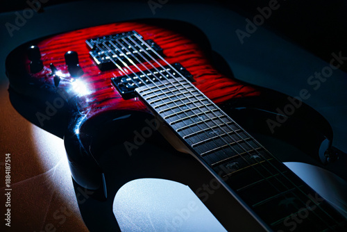 A red electric guitar with sunburst finish, sitting on a flat surface The glossy body curves around the neck and reflects light from above Strings are visible over a pickguard
