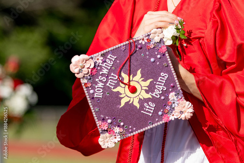 Valokuva A high school or college graduate holds her decorated cap reading now's when my life begins — a joyful, personal image of commencement, achievement, and life's next chapter