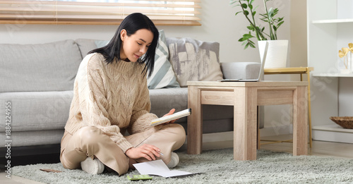 Fotografia Young woman with notebook calculating refund at home