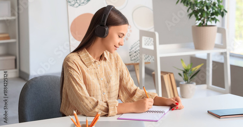Teenage girl with headphones studying at table in room