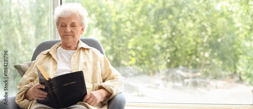 Senior woman in armchair reading Bible at home
