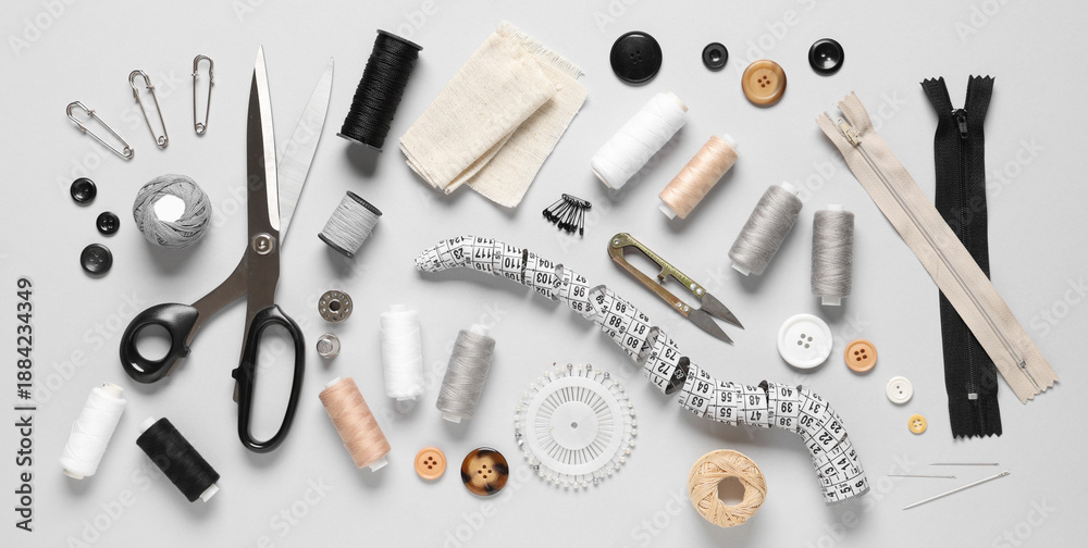 Fototapeta premium Set of thread spools with fabric, measuring tape, scissors and sewing supplies on grey background