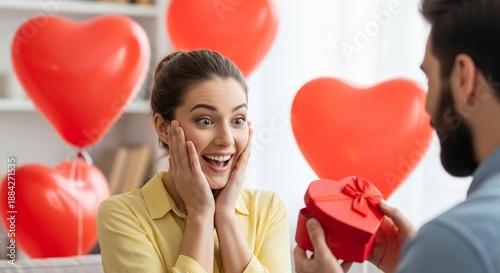 Surprised woman joyfully accepts a romantic heart-shaped gift from her loving partner, surrounded by celebratory red balloons, capturing a special moment of affection and happiness
