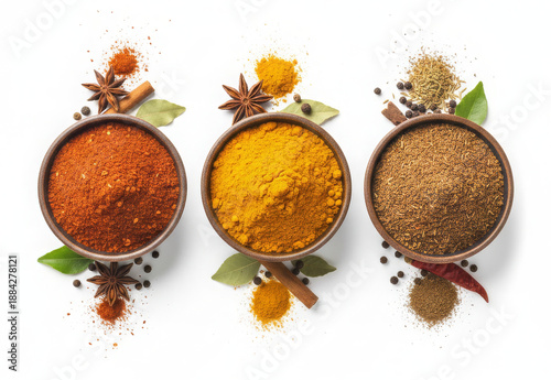 Assorted spices in clay bowls including turmeric, chili powder, and cumin, with star anise and leaves. Top view on white