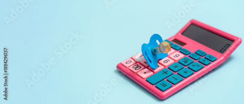 A baby pacifier lies on a calculator on a blue background, the concept of the cost of childbirth and child care benefits