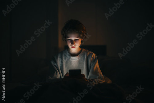 teenager sitting on bed illuminated only by smartphone light, Teen digital isolation concept