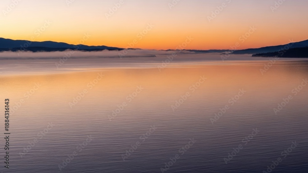 Fototapeta premium Misty water, distant mountains at dawn, gradient orange/purple colors abound