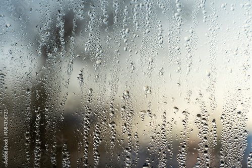 Raindrops and condensation on window glass with blurred outdoor background. Close-up texture photography. Rainy weather and moisture concept for design, banner, poster, wallpaper. Macro shot with copy