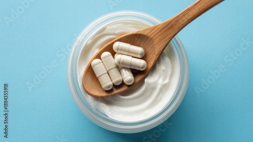 Probiotic capsules on a wooden spoon resting on a container of white yogurt against a blue background.