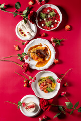 Gourmet dishes and desserts elegantly arranged on a vibrant red background with fresh strawberries and red roses, ideal for romantic dinner, Valentine's Day, or fine dining concepts.