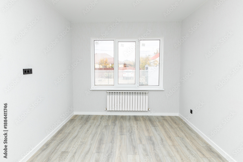 Obraz premium Empty interior room after renovations with white freshly painted walls and big window, allowing natural light, with a wooden floor, a radiator beneath the windows