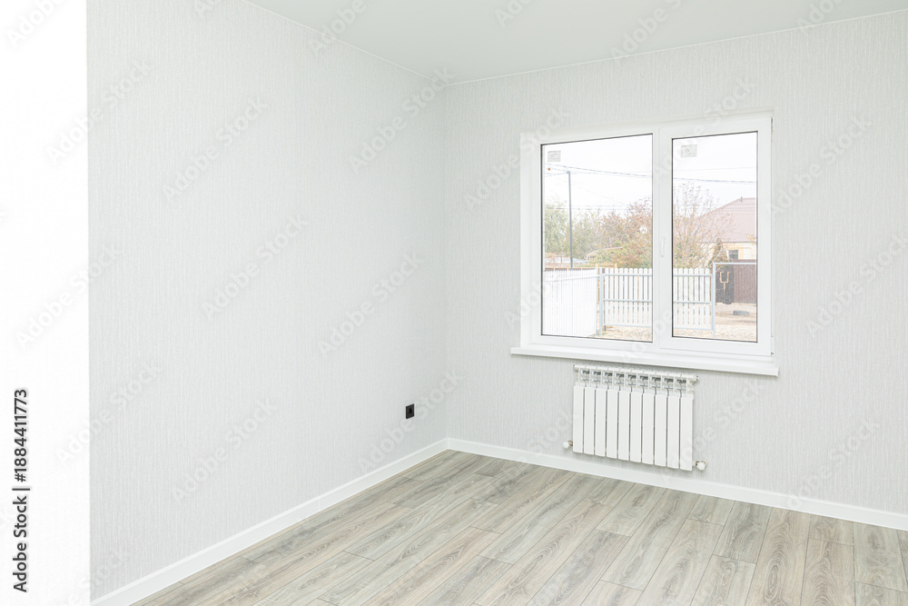 Fototapeta premium Empty interior room after renovations with gray freshly painted walls and big window, allowing natural light, with a wooden floor, a radiator beneath the windows