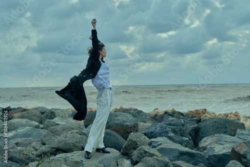 Φωτογραφία Woman on rocky shore with ocean horizon, wind in motion, celebrating achievement and freedom in outdoor attire, confident stance by water and sky and light