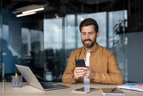 Bilde på lerret Smiling man concentrating on his smartphone while sitting at a modern office des