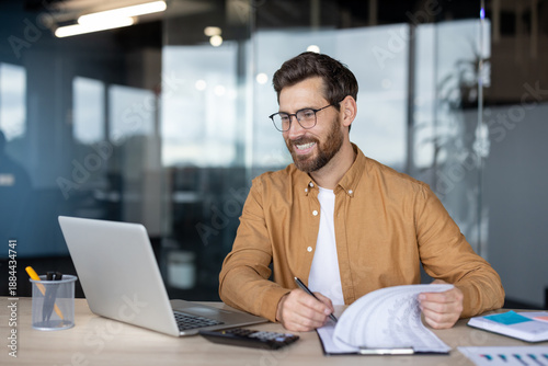 Tableau sur toile Smiling professional man wearing glasses concentrating on his work at a desk, re