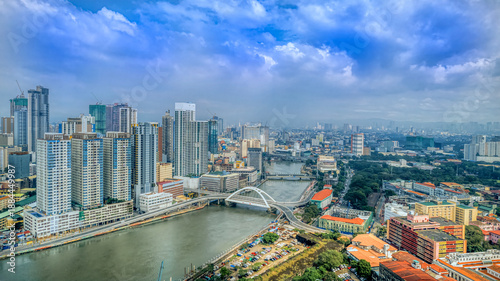 Aerial view of Manila city in the Philippines showing a dense skyline, river, and modern bridge beneath dramatic clouds, representing urban development, infrastructure, and metropolitan scale.