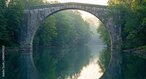 Ancient stone arch bridge spans tranquil waterway surrounded by dense verdant forest in soft morning light