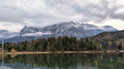 A beautiful cinematic shot of a calm mountain lake with a crystal reflection of majestic peaks hidden in clouds.