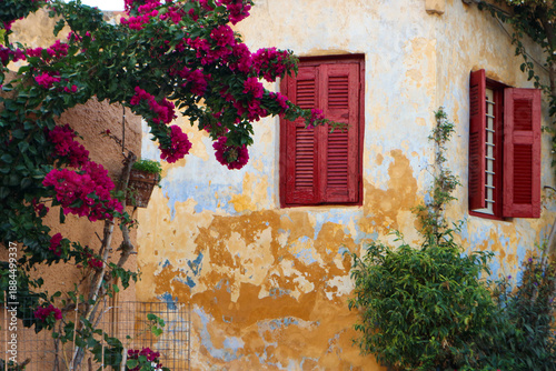 Anafiotika house in Athens, with old yellow walls, red shutters and bougainvillea flowers