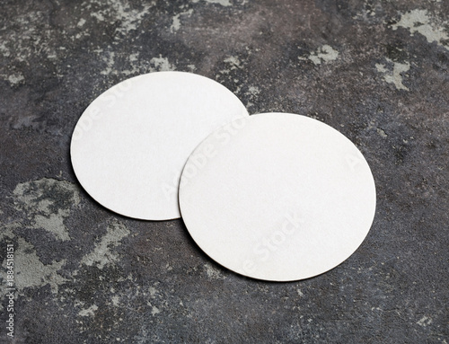 Two blank beer coasters on concrete surface.