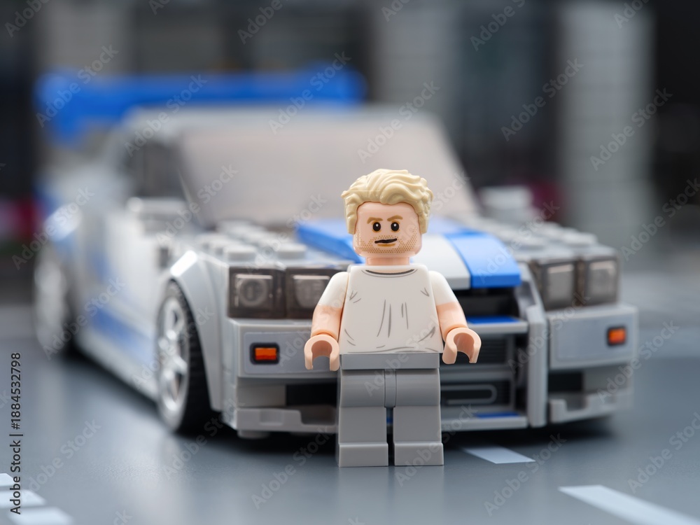 Fototapeta premium Tambov, Russian Federation - August 21, 2025 Lego Brian O'Conner minifigure standing in front of his Nissan Skyline GT-R (R34) car in city street. 2 Fast 2 Furious movie. Lego Speed Champions.