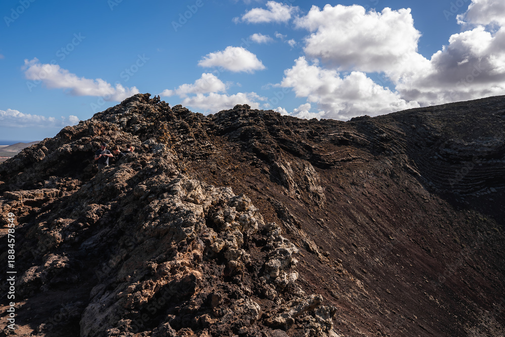 Naklejka premium A rugged volcanic ridgeline forms a crater crest in Timanfaya, Lanzarote, Canary Islands. Layered lava strata show in daylight with deep shadows and no vegetation.