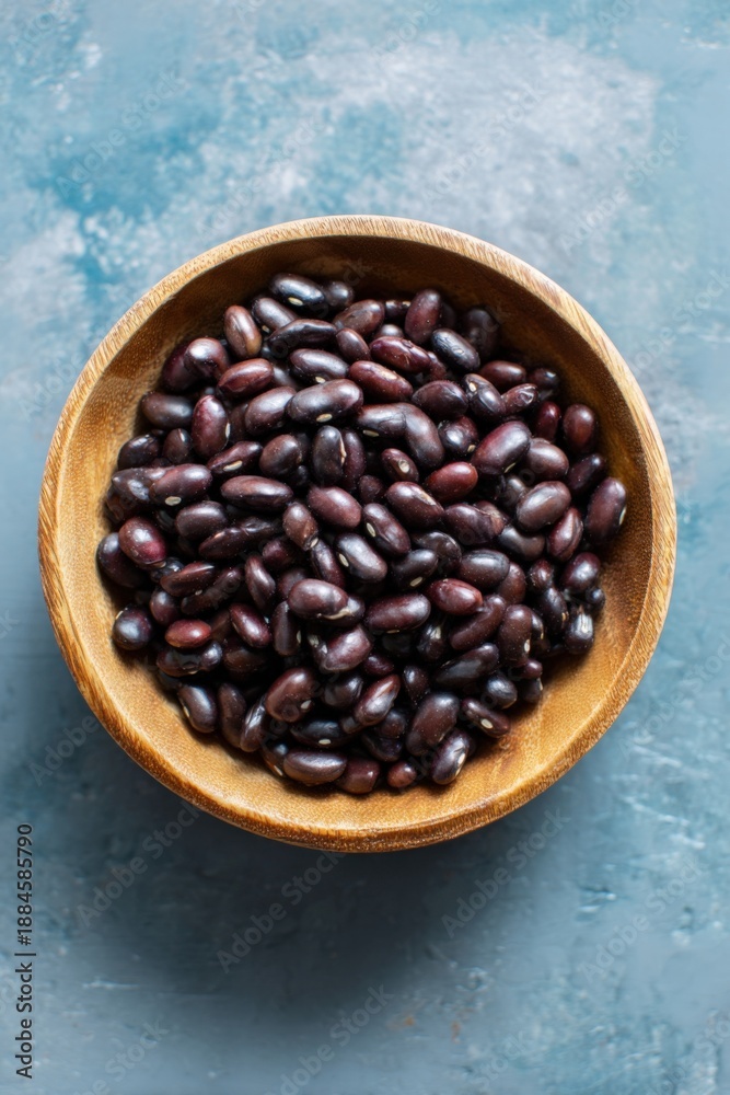 Fototapeta premium Wooden bowl of raw black beans on textured blue surface